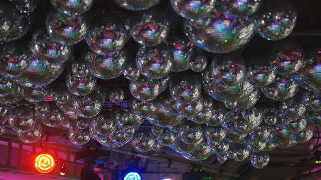 一个反射的迪斯科球。他们悬挂在舞台上方的天花板上，被不同的灯光照射着视频素材