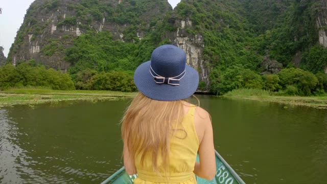 在越南北部的旅游胜地宁平，一名年轻女子在船上在壮观的石灰岩中漂流。去越南旅游的概念视频素材