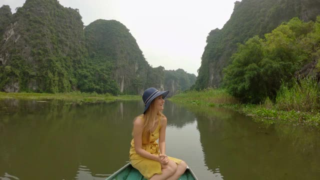 在越南北部的旅游胜地宁平，一名年轻女子在船上在壮观的石灰岩中漂流。去越南旅游的概念视频素材