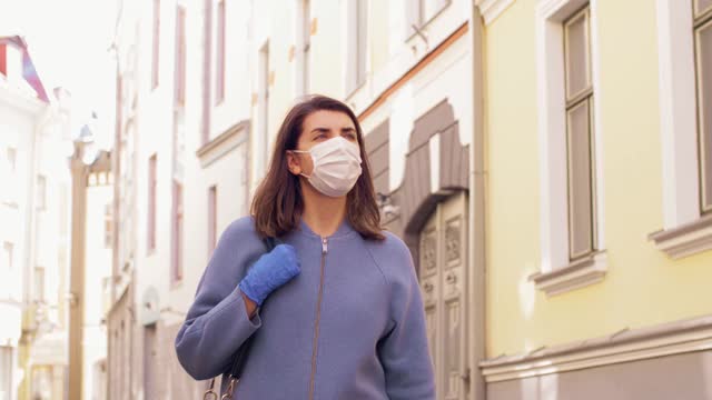 戴着医用口罩和手套的女人走在城市里视频素材