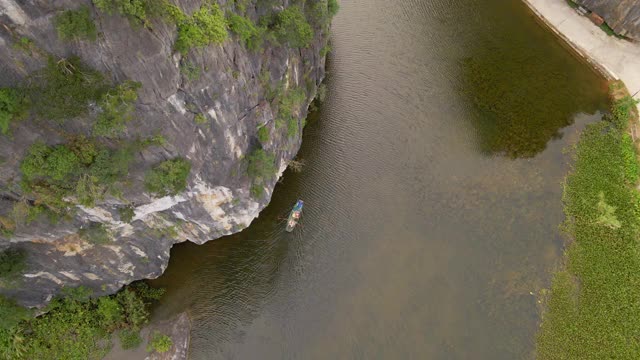 这是越南北部著名的旅游景点宁平地区美丽的石灰岩山脉的航拍照片。去越南旅游的概念。一个当地人在船上顺流而下视频素材