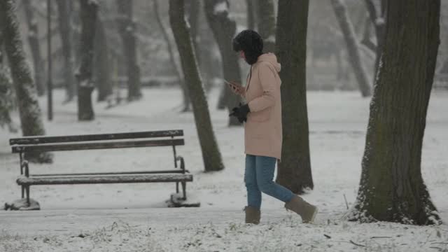 在寒冷的冬天，一名女子在公园里边走边打电话视频素材