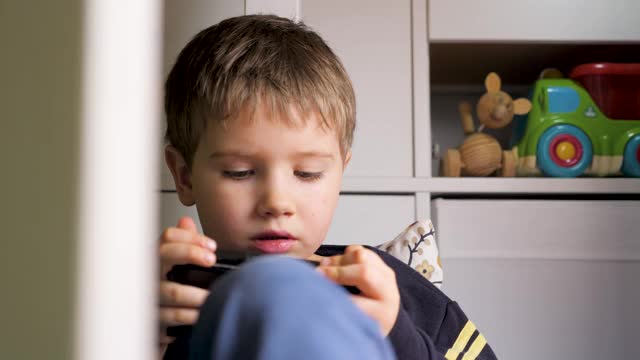 孩子们不喜欢小玩意。小男孩在智能手机上玩游戏。男孩使用智能手机。孩子在玩手机游戏。儿童使用的小工具。一代α。孩子在玩手机。新一代视频素材