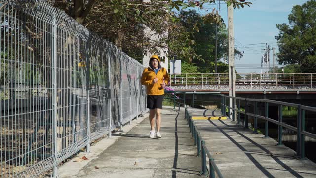 亚洲年轻的跑步者男子穿着毛衣兜帽听音乐在公园在早上在户外。适合男性慢跑锻炼。运动训练视频素材