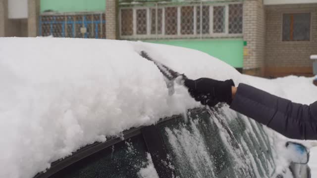 一位妇女用刷子清理汽车上的积雪。视频素材