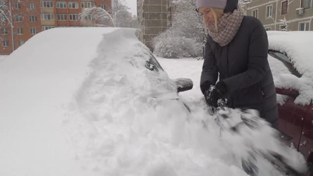 一位妇女用刷子清理汽车上的积雪。视频素材