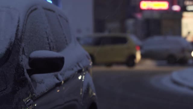 在夜晚的降雪中，汽车在覆盖着积雪的城市道路上行驶。高速公路上有发生事故的危险。飓风期间的艰难道路状况视频素材