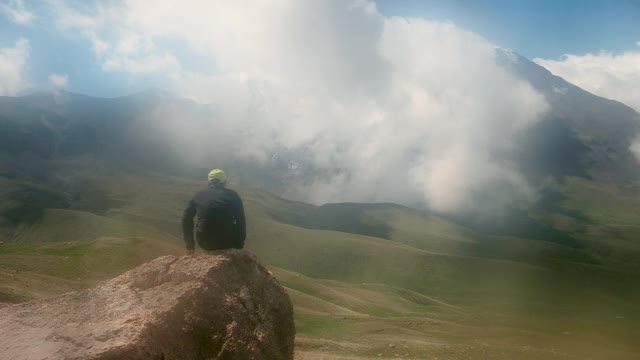 旅行的生活方式。生存的概念。游客坐在石头上。向远方挥手。徒步旅行。有雾，雨天，后视镜。岩石、山。体育运动。视频素材