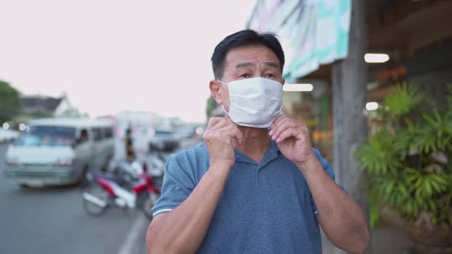 亚洲中年男子戴着医用口罩站在街边，预防新冠肺炎大流行期间的传染病视频素材