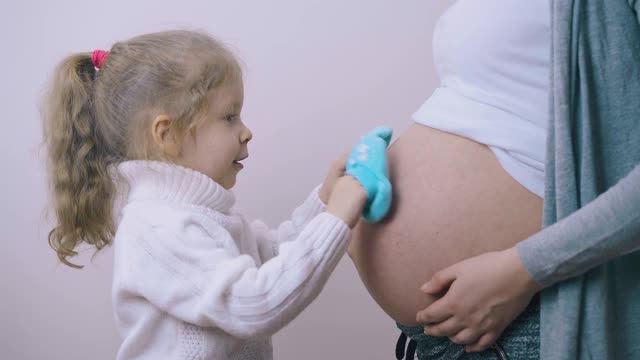 漂亮女孩用蓝色的靴子摸着怀孕妈妈的肚子视频素材