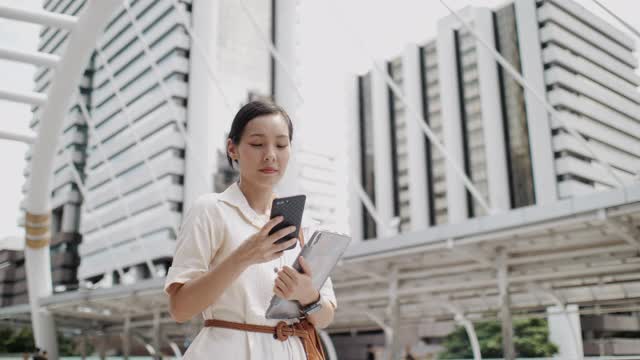 亚洲女性在城市户外行走时用智能手机看屏幕视频素材