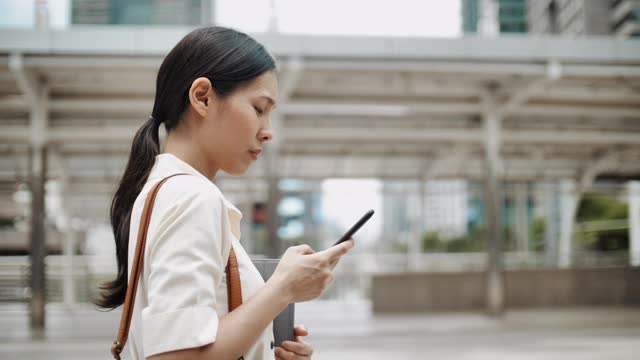 亚洲女性在城市户外行走时用智能手机看屏幕视频素材