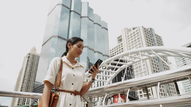 亚洲女性在城市户外行走时用智能手机看屏幕视频素材