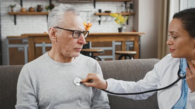 女医生检查老年男子的帮助下，听他的肺，坐在沙发上医疗咨询在家视频素材