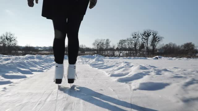 穿着白色花冰鞋的职业女滑冰运动员正在结冰的湖面上滑冰。冬天，女人的脚在河上滑冰。冬天滑冰活动视频素材