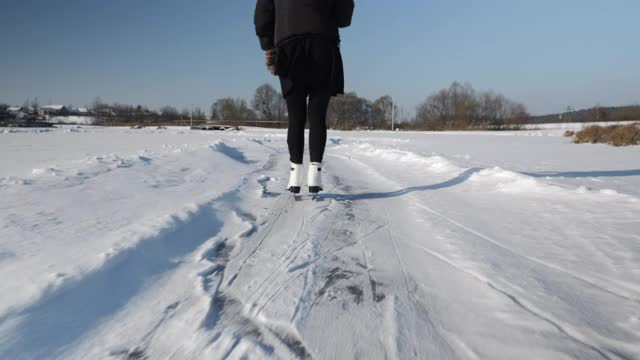 女性的脚在白雪覆盖的湖面上滑冰。冬天，穿着白色花样滑冰鞋的妇女在结了冰的池塘上滑冰。冬季户外活动视频素材