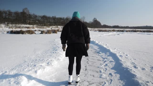 女人独自在结冰的湖面上滑冰。女人们穿着白色的花样滑冰鞋在结冰的池塘上滑行。冬季运动活动视频素材