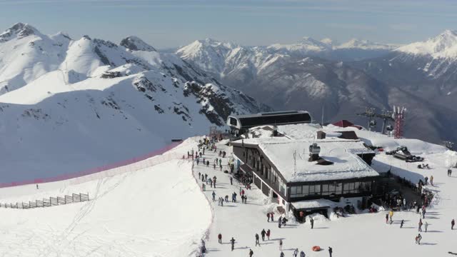 冬季滑雪胜地鸟瞰图。冬季，滑雪者和滑雪板游客在山顶村庄。在阳光充足的雪坡上有滑雪缆车的山区度假胜地。4 k鸟瞰图视频素材