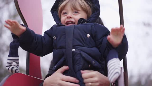 2019冠状病毒病冬季期间，幼儿与母亲在操场上玩耍。孩子滑下雪橇视频素材