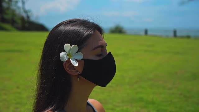 一个欧洲的黑发女孩独自练习瑜伽在大自然中坐在草地上莲花姿势戴着一个黑色的保护面罩和她的耳朵后面的一朵白色的花视频素材