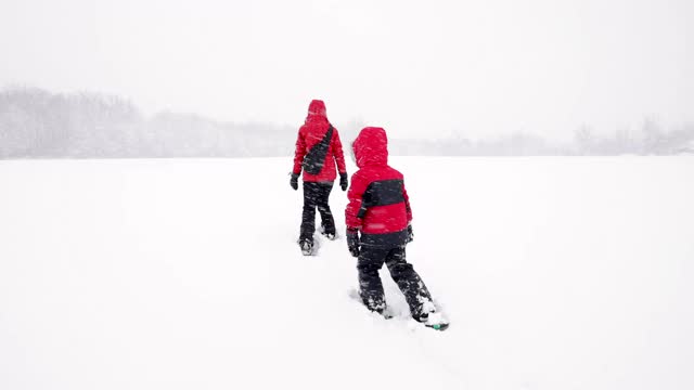 母亲和儿子在冬天雪鞋户外在暴风雪视频素材