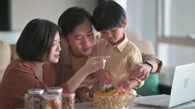 亚洲华人家庭在客厅里装饰，在生日蛋糕上插入生日蜡烛，准备和爷爷奶奶视频通话庆祝生日视频素材