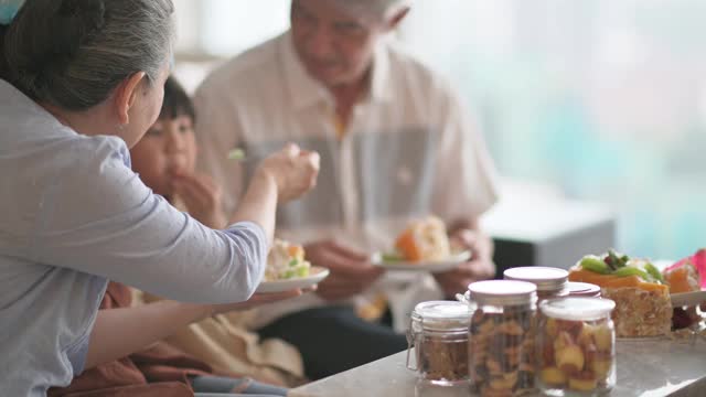 亚洲华人多代同堂庆祝生日，孙子戴着派对帽在客厅吃生日蛋糕视频素材