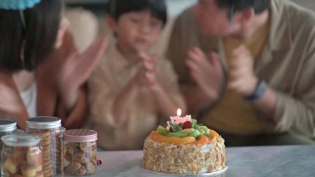 亚洲华人家庭在家里庆祝生日，儿子戴着派对帽，在生日蛋糕前唱歌、鼓掌和祝福视频素材