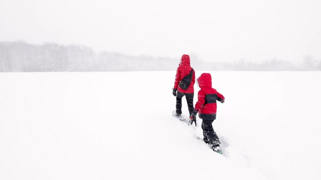 母亲和儿子在冬天雪鞋户外在暴风雪视频素材