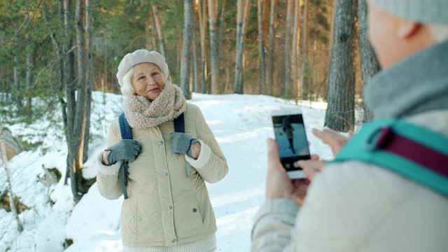 快乐的老年游客女士摆姿势为智能手机相机在雪天公园在冬天视频素材