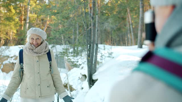 快乐的老女人徒步旅行者摆姿势的相机，而丈夫与相机在森林在冬天拍照视频素材