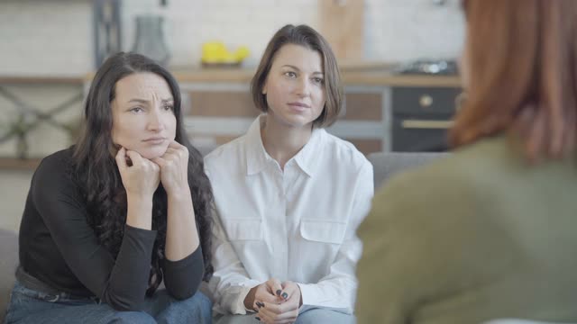 年轻的白人女人在前面跟一个认不出来的模糊的朋友抱怨。支持美丽的女士安抚悲伤的压力红发女人。支持和友谊。视频素材