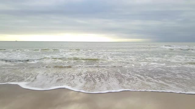 鸟瞰图与接近的海浪，白色的浪花在日落的海滩视频素材