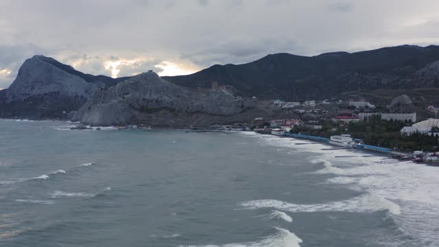 从无人机在度假城市的山海湾景观。苏达克山脉，海浪拍打着海滩。鸟瞰图高地上的城市背景视频素材