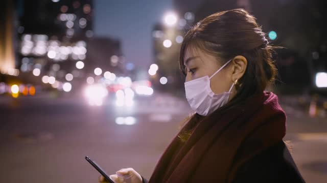 女商人晚上在城市等待路灯时使用智能手机并戴上防护口罩视频素材