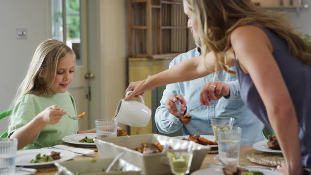 父母为家人提供食物，在家里围坐在桌子上一起享受晚餐视频素材