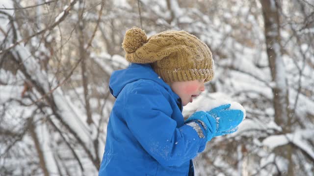 孩子吹着手中的新雪。小男孩在玩新鲜的雪。在大雪纷飞的冬日，孩子们活跃的户外休闲活动。视频素材