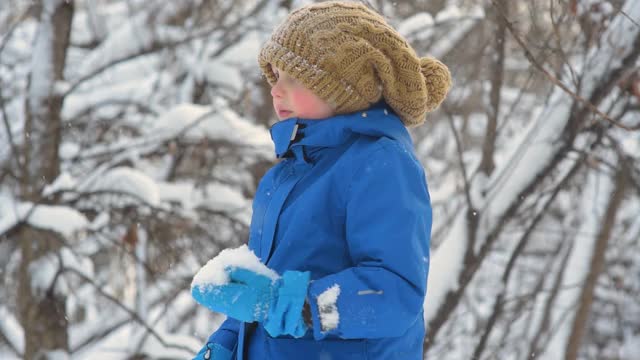 孩子吃新鲜的雪躺在他的手中。小男孩在玩新鲜的雪。在大雪纷飞的冬日，孩子们活跃的户外休闲活动。视频素材