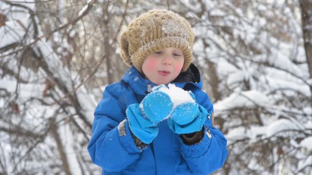 孩子吹着手中的新雪。小男孩在玩新鲜的雪。在大雪纷飞的冬日，孩子们活跃的户外休闲活动。视频素材