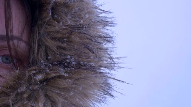 一个穿着毛皮兜帽的女孩在暴风雪中，雪花飘落，凝视前方，冰冷。近距离观察眼睛视频素材