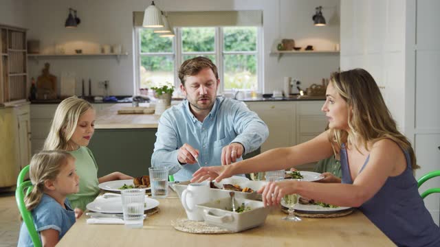 父母为家人提供食物，在家里围坐在桌子上一起享受晚餐视频素材