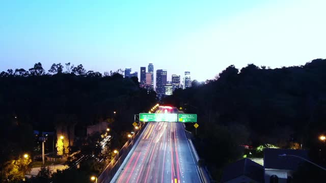 从黄昏到夜晚的洛杉矶高速公路交通的空中时间流逝，以市中心天际线的城市灯光为背景视频素材