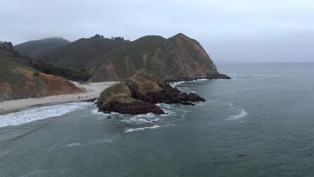 空中拍摄的海浪溅在锁眼拱对天空，无人机飞向游客在海滩-大苏尔，加利福尼亚视频素材