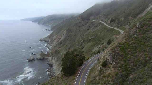 航拍车辆在海上蜿蜒的山路上，无人机在雾霾天气下飞越海岸线-大苏尔，加利福尼亚视频素材