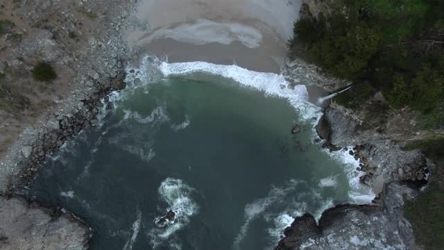 从岩石飞溅在海滩上的瀑布鸟瞰图，无人机上升在岸上的岩石形成-大苏尔，加利福尼亚视频素材