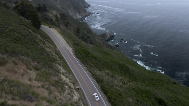 空中倾斜拍摄在海上山路上的汽车与天空的对比，无人机在植物和树木上向前飞行——大苏尔，加利福尼亚视频素材