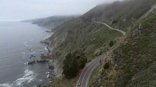 空中封锁拍摄在海上蜿蜒山路上的车辆，无人机在雾霾天气下飞越海岸线——大苏尔，加利福尼亚视频素材