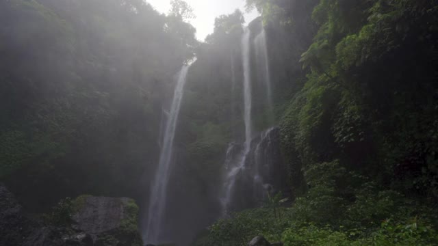 慢镜头倾斜沿着冲下的瀑布在迷雾中的雨林与岩石和茂盛的热带植物-巴厘岛，印度尼西亚视频素材