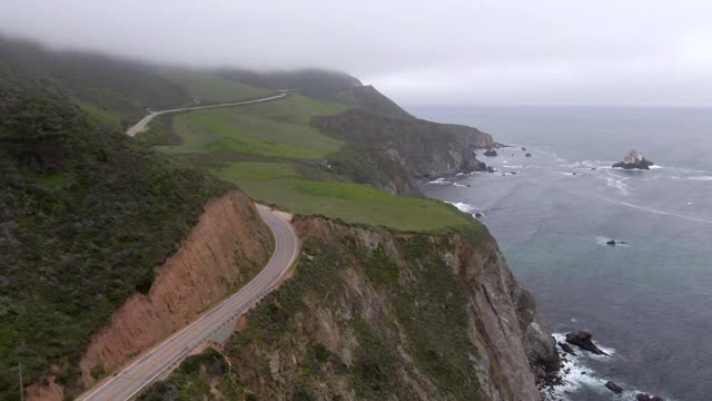 航拍海浪溅在岩石悬崖附近的车辆，无人机在雾天气期间向前飞行的海岸线-大苏尔，加利福尼亚视频素材