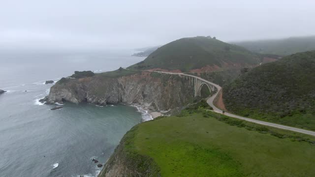 空中倾斜向下拍摄的比克斯比溪桥与汽车从海上对着天空，无人机在雾天气海岸线上向前飞行-大苏尔，加利福尼亚视频素材